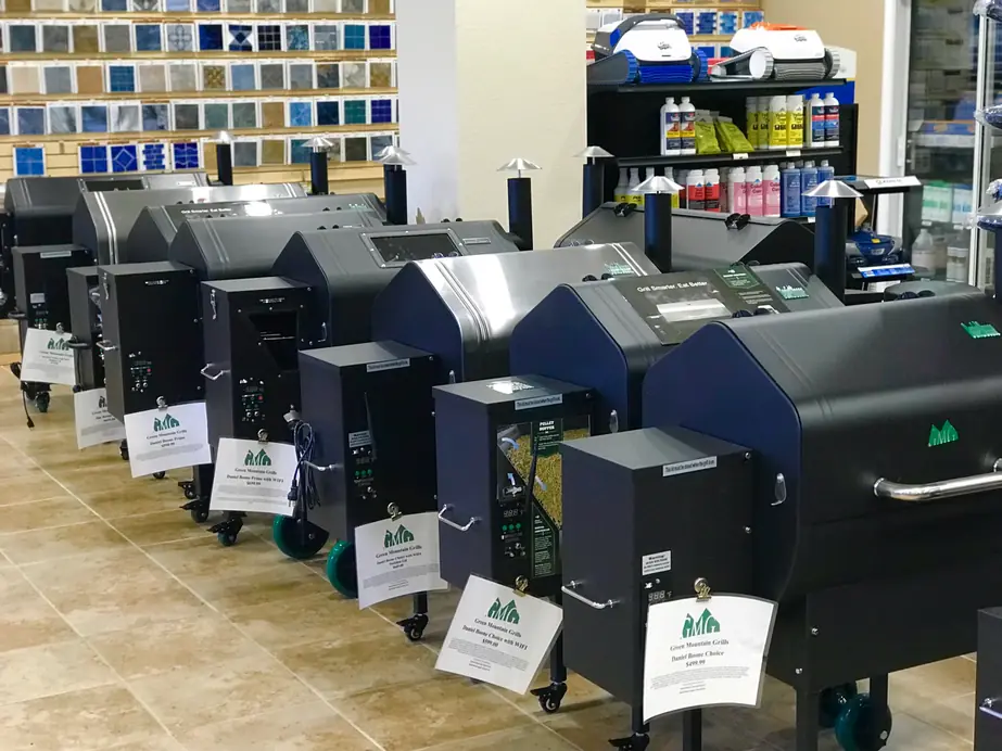 Showroom wall of pool chemicals and tile samples above a row of pellet grills
