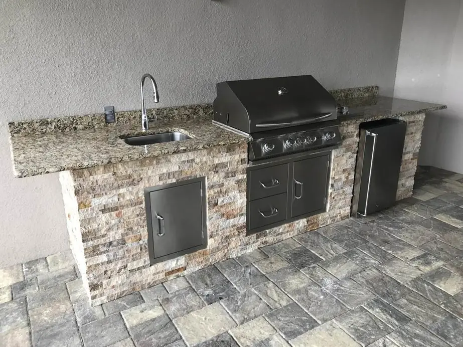 Built-in outdoor kitchen with a stacked-stone base, granite top, stainless grill and sink