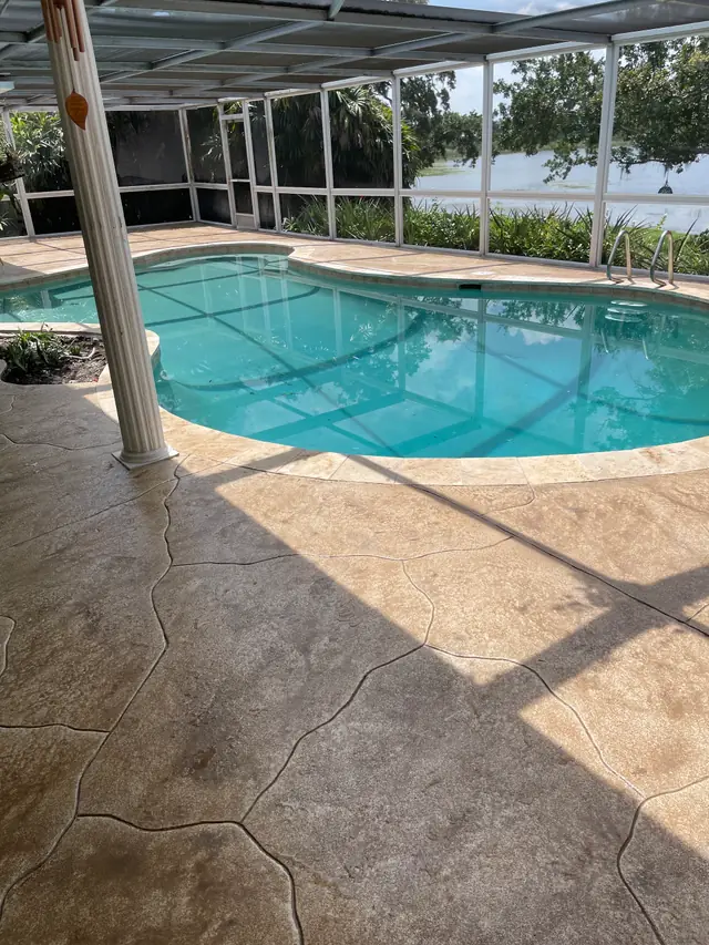 A screened pool with a textured deck surround and a lake beyond the screen