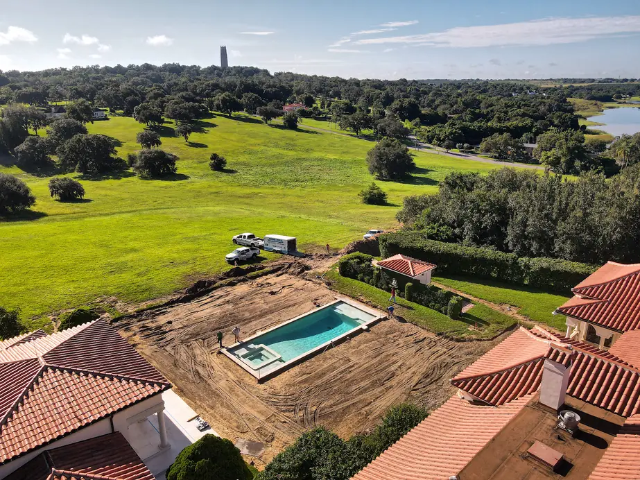 Aerial view of a new pool shell going in beside a tile-roof home on a golf course