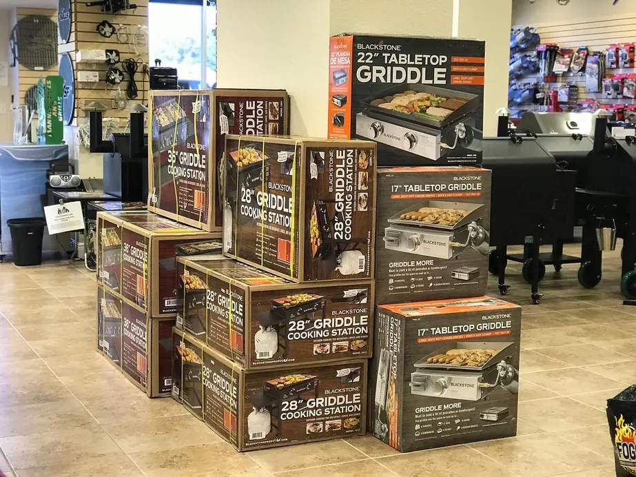 Boxed Blackstone griddles stacked on the showroom floor beside a Traeger