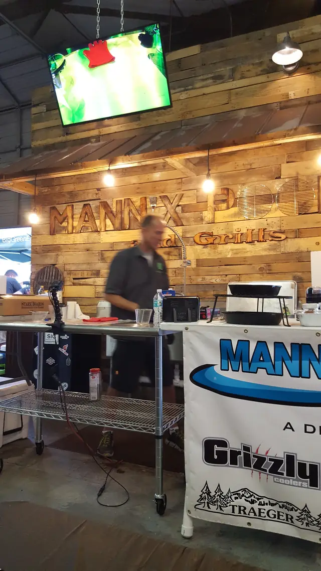 A Mannix Pools and Grills event booth with a wood-panel backdrop and a pellet grill demo